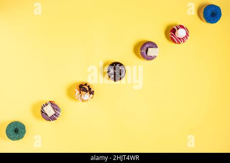 Colorful donuts or doughnuts in various shapes on yellow bright background. Colorful and happy image and concept. Stock Photo