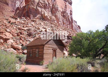 The tiny small Fruita Schoolhouse with the red rock cliff on the back in Utah Stock Photo