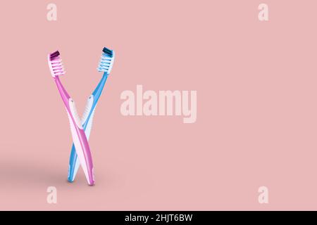 Creative idea made of two toothbrushes pink and blue bristles in an embrace, isolated on bright pink background. Copy space. Stock Photo