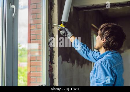 Man in a blue shirt does window installation. Using a mounting foam Stock Photo