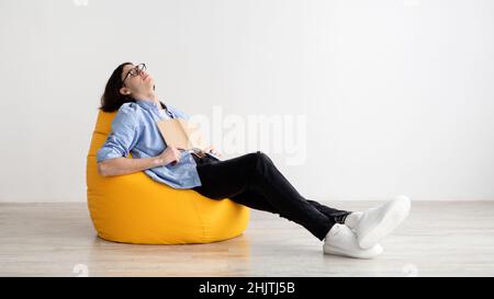 Remote education concept. Bored male student sleeping with book, sitting in beanbag chair, panorama, free space Stock Photo