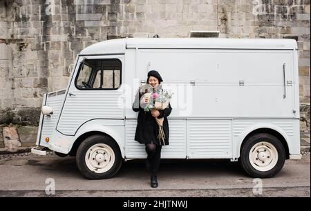 Asian woman leaning on a truck holding flowers and coffee Stock Photo