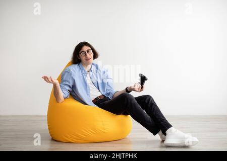 Bored man sitting in beanbag chair with joystick, playing video games alone and losing, resting at home, free space Stock Photo