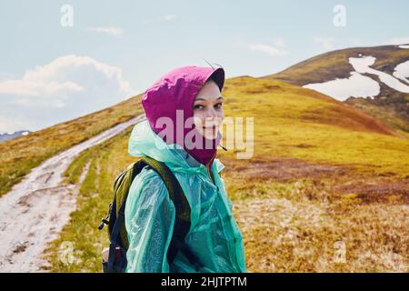 Woman in a raincoat against the backdrop of a mountain peak. Stock Photo