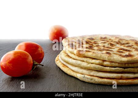 Flatbread with cheese and herbs on a dark stones plate with tomatoes Stock Photo