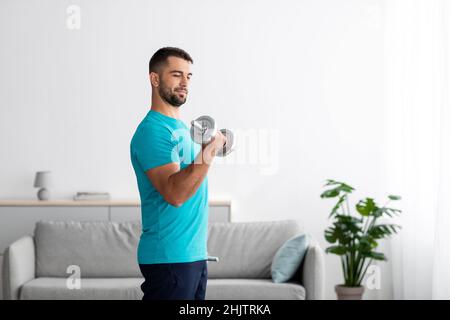 Concentrated serious millennial european guy doing strength exercises for arms and lifting dumbbells Stock Photo