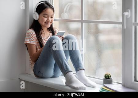 Happy chinese child using headset and smartphone at home Stock Photo