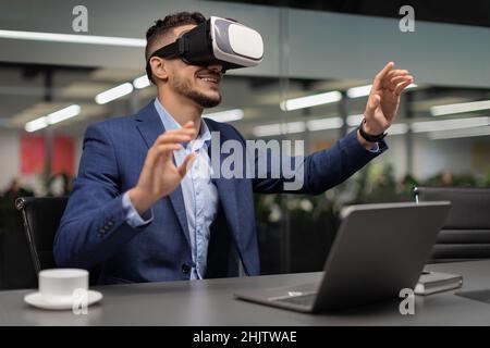 Excited businessman sitting at workdesk, using VR glasses Stock Photo