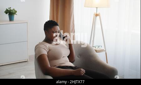 Pleasure conversation. Young positive chubby african american woman talking to friends via mobile phone and smiling Stock Photo