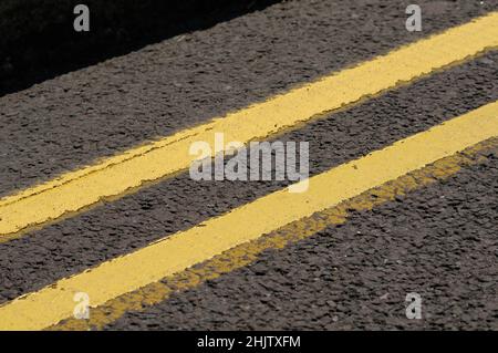 Close-up of double yellow lines painted on the road surface in a UK street indicating no waiting or parking at any time. Stock Photo