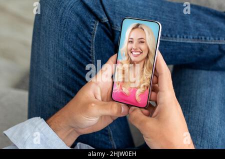 Unrecognizable man using smartphone and having video call with attractive lady girlfriend, sitting at home Stock Photo