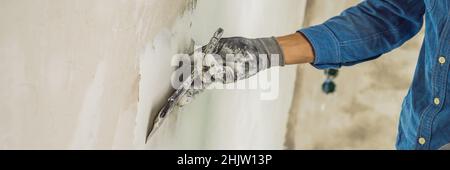 master is applying white putty on a wall and smearing by putty knife in a room of renovating house in daytime BANNER, long format Stock Photo