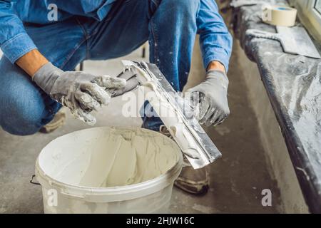 master is applying white putty on a wall and smearing by putty knife in a room of renovating house in daytime Stock Photo