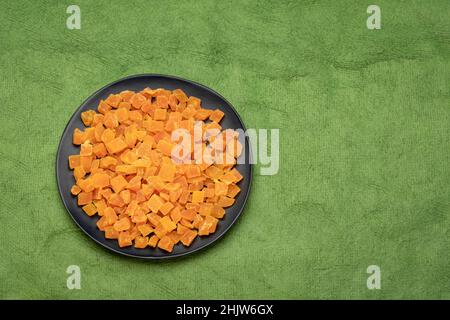dried mango fruit diced - black ceramic palte on a green textured paper with a copy space Stock Photo