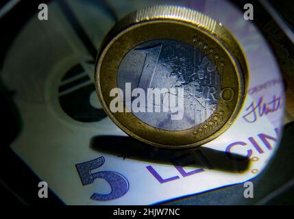 Bucharest, Romania - February 02, 2022: One EURO coin and its equivalent in Romanian lei, a 5 lei banknote, photographed through a magnifying glass. T