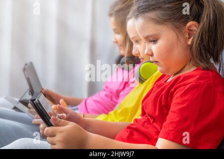 Children girls sitting together on the couch and carefully look at the tablets Stock Photo