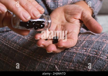 Elderly caucasian woman spilling out black tablets.  Stock Photo
