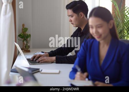 Asian businessman concentrated working on laptop computer at his desk, in the office room with his colleagues. businesspeople concept Stock Photo