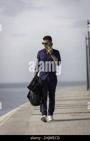 Young male walking alone and using the smart phone along the Lisbon riverside Stock Photo