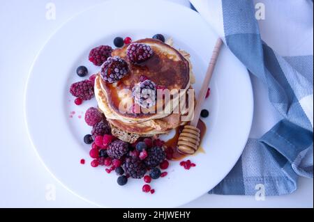 Pancakes with berries and honey on white table Stock Photo