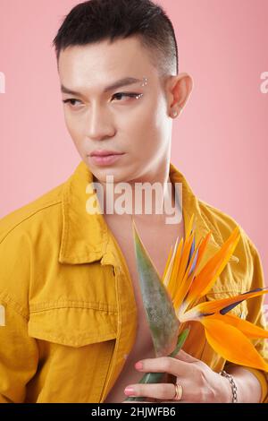 Portrait of young man with rhinestones on face holding crane flower and looking away Stock Photo