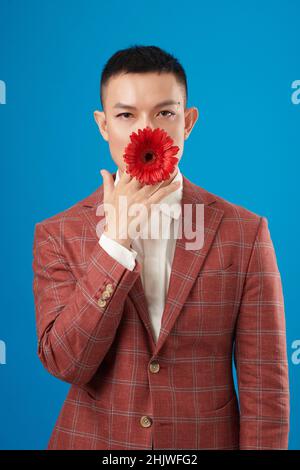 Portrait of young man in plaid suit jacket putting red blooming flower in mouth Stock Photo