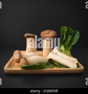 Popular uncooked healthy asian edible King Oyster mushrooms and Baby Bok Choy on wooden plate on black background. Stock Photo