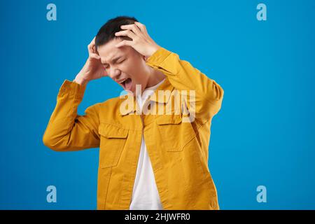 Emotional young man touching his head and shouting in despair Stock Photo