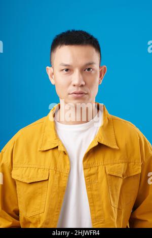 Serious young man in casual closed looking at camera, isolated on blue Stock Photo