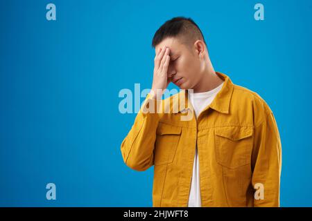 Tired disappointed young man making face palm gesture, isolated on blue Stock Photo