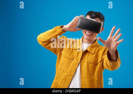 Positive young man testing new application for virtual reality headset, isolated on blue Stock Photo