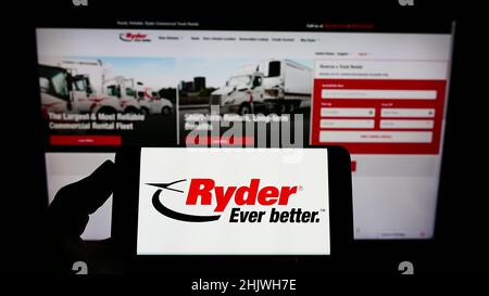 Person holding smartphone with logo of US transportation company Ryder System Inc. on screen in front of website. Focus on phone display. Stock Photo