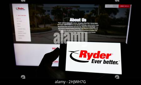 Person holding mobile phone with logo of American transportation company Ryder System Inc. on screen in front of web page. Focus on phone display. Stock Photo