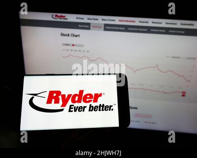 Person holding cellphone with logo of US transportation company Ryder System Inc. on screen in front of business webpage. Focus on phone display. Stock Photo