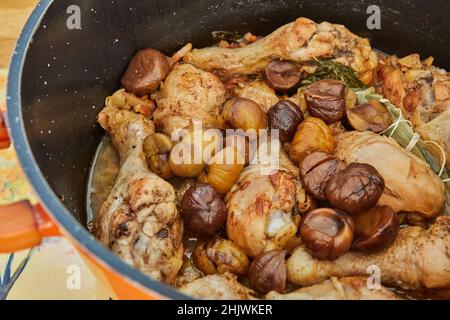 Chicken legs baked with chestnuts and mushrooms in saucepan on gas stove. French gourmet cuisine Stock Photo
