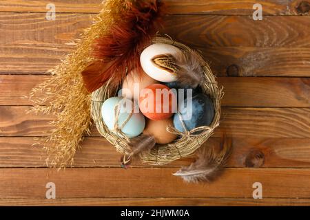 Nest with multicolored Easter eggs, feathers and spikelets on wooden background Stock Photo
