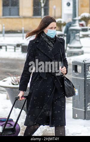Elegant beautiful business girl wearing black jacket with protective medical mask and luggage walking in the street during Covid or Coronavirus Stock Photo