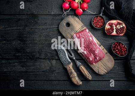 Raw beef fillet steaks with herbs and spices with whole tenderloin fillet cut set, in cast iron frying pan, on black wooden table background, top view Stock Photo