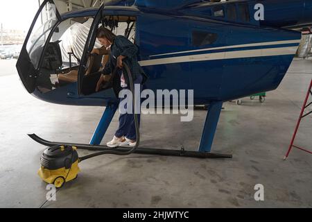 Young woman using vacuum cleaner while working in cockpit of airplane Stock Photo