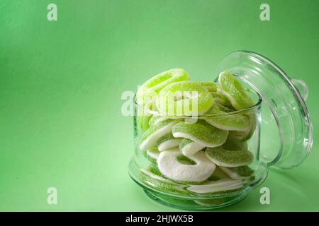 Chewy sweets and apple flavoured gummy candy concept with close up on sweet and sour green rings covered in granulated sugar in a clear glass jar isol Stock Photo