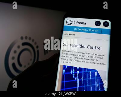 Person holding smartphone with webpage of British publishing company Informa plc on screen in front of logo. Focus on center of phone display. Stock Photo