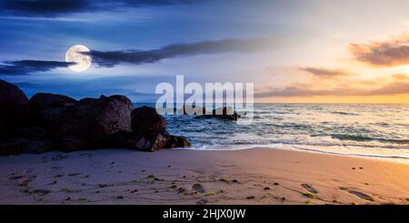 day and night time change concept above huge stones on the sandy beach at twilight. wonderful velvet season vacation. clouds on the blue sky with sun Stock Photo