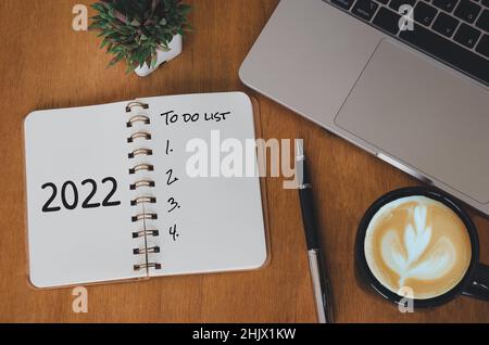 computer laptop Notebook and pen and cactus with coffee cup on desk.Top view to do list 2022 new year. Stock Photo