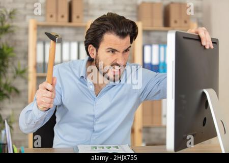 angry businessman holding hammer over laptop in his office Stock Photo