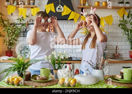 Mom and daughter have fun joking with eggs while preparing for Easter. Stock Photo