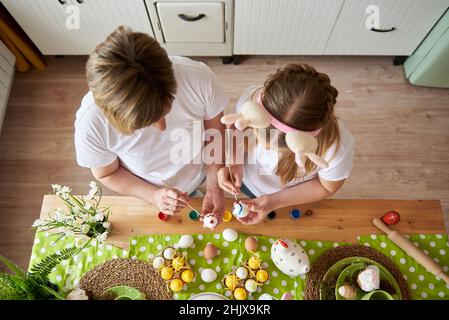 Mom and daughter are preparing for Easter and painting eggs with brushes, top view. Stock Photo