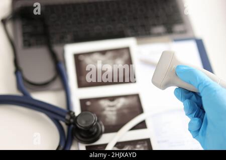 Doctor holding ultrasound probe against background of pictures and medical documents closeup Stock Photo