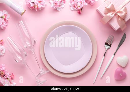 Place setting for Valentine's Day. Romantic dinner, table setting with cutlery. Pink background. Dating concept, love. Spring flowers, empty plate, gl Stock Photo