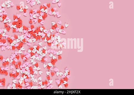 Red and white heart shaped sugar dessert sprinkles on pink background with copy space Stock Photo