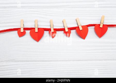 Red hearts with clothespins hanging on clothesline isolated on white wooden background. Valentinas day Stock Photo